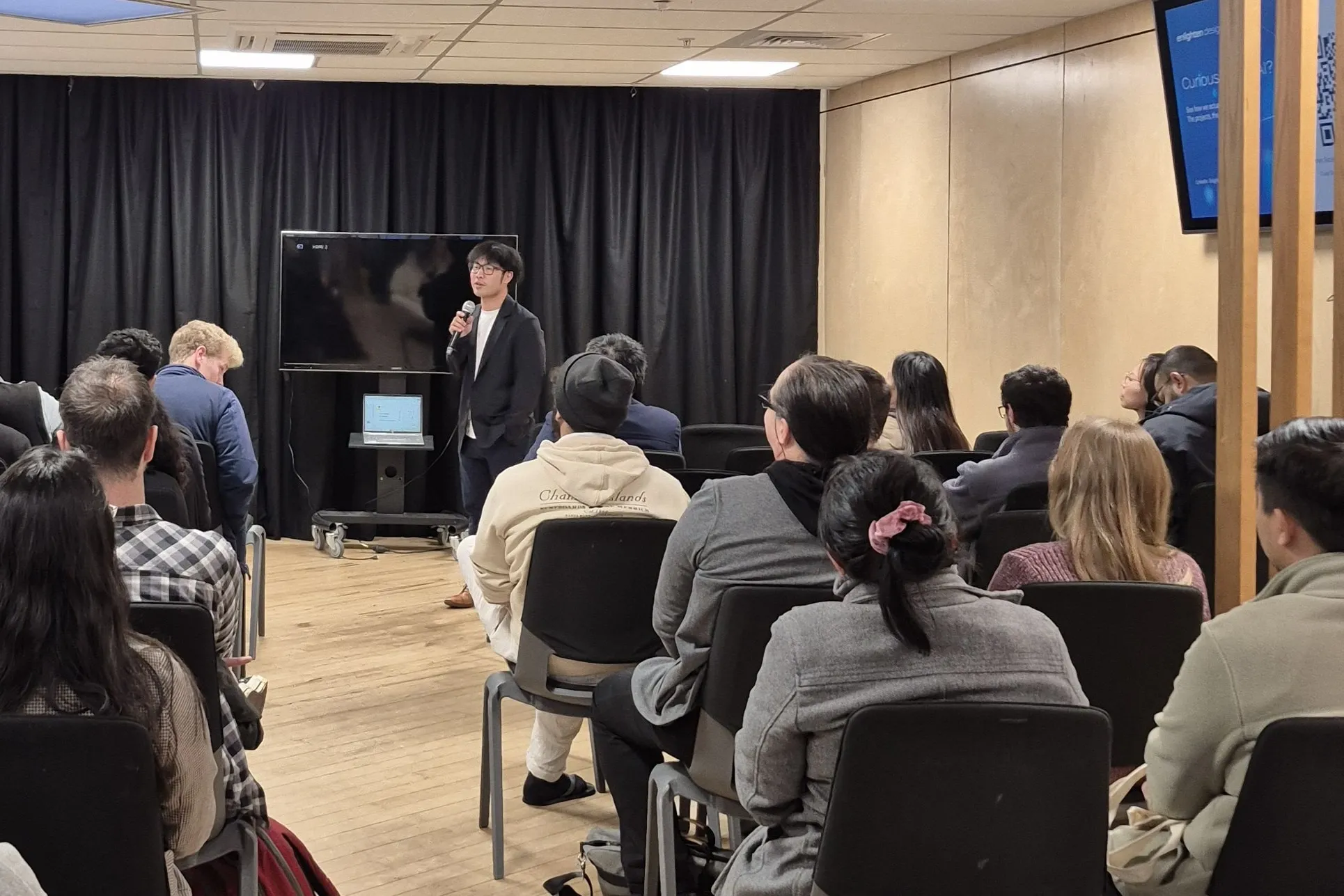 Re:Gen AI, July 2026, University of Waikato: Benny at the microphone, seen from the back of a full room